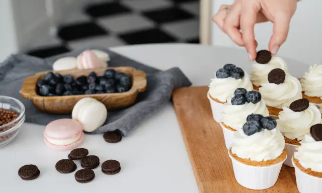 Des cupcakes décorés avec une crème chiboust aérienne, des myrtilles et des biscuits. Des macarons et des myrtilles sont disposés à côté.