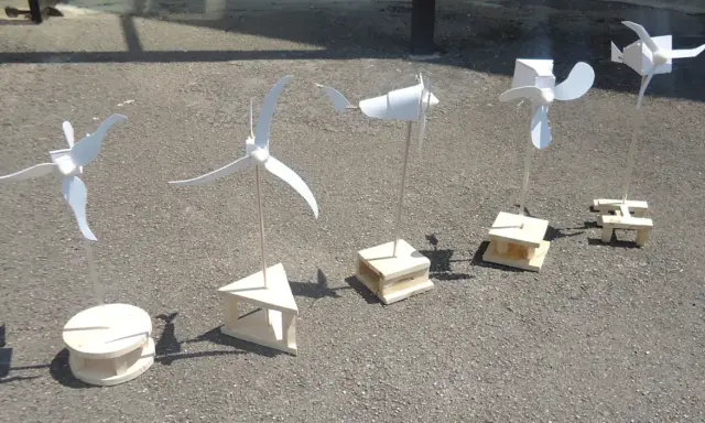 Cinq maquettes éoliennes, fabrication simple en bois, alignées sur un sol gris.