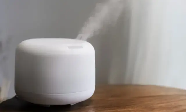 Humidificador casero blanco emitiendo vapor sobre una mesa de madera.