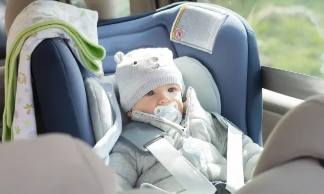 Bebé con gorro de oso y chupete en un alzador o silla coche, listo para un viaje seguro.