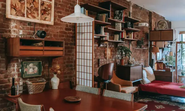 Wnętrze kawalerki z ceglaną ścianą, drewnianym stołem i meblami w stylu vintage.
