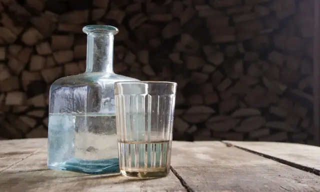 Szklanka i butelka z płynem na drewnianym stole. Czy to bimber? Co to jest?