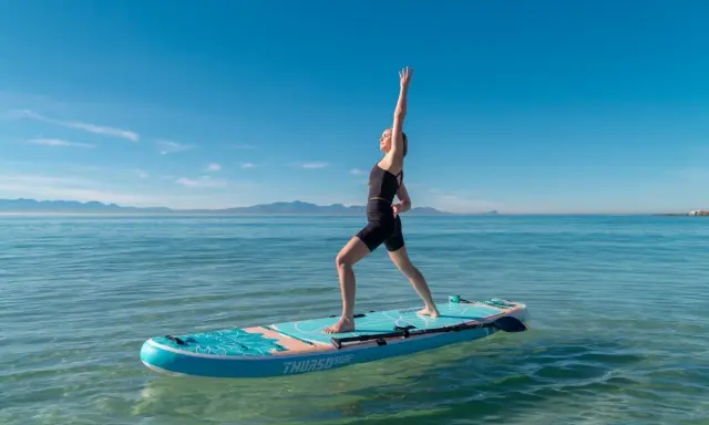 Kvinna utövar sup yoga på en paddleboard i lugnt vatten med berg i bakgrunden.