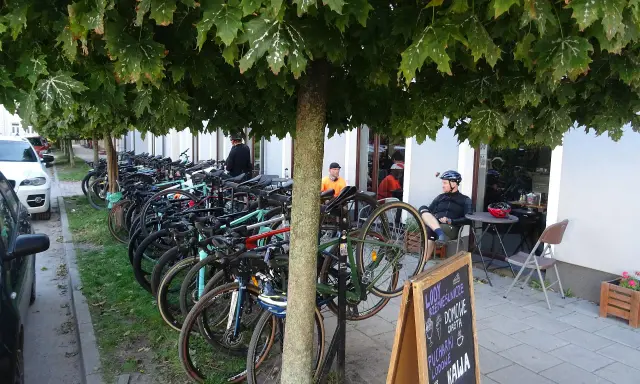 Rowerzyści odpoczywają pod drzewami w Górze Kalwarii. Rzędy rowerów czekają na dalszą trasę.
