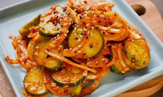 Pikantne ogórki po koreańsku, pokrojone w plasterki i wymieszane z cebulą, posypane sezamem.