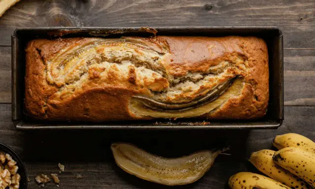Un delizioso banana bread light appena sfornato, con banane caramellate in superficie, su un tagliere di legno.