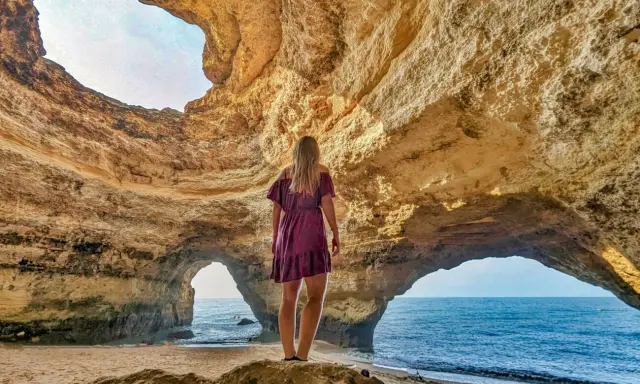 Frau steht in Höhle, blickt auf Meer. Ein Highlight der Algarve.