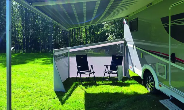 Ett vindskydd från Biltema ger skugga och skydd vid husbilen. Två stolar står redo för avkoppling i gräset.
