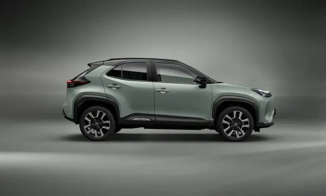 Nowy, zielony toyota crossover Yaris Cross z czarnym dachem i felgami stoi na szarym tle.
