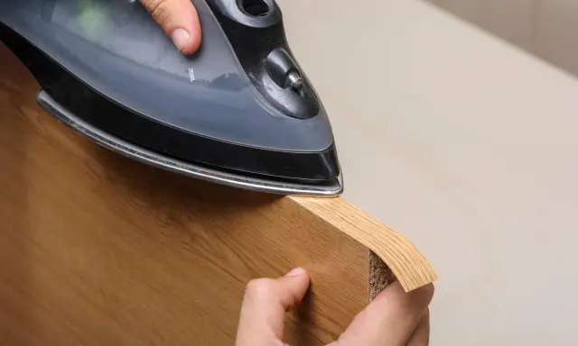 Persona aplica cinta de cantear a un borde de madera con una plancha.