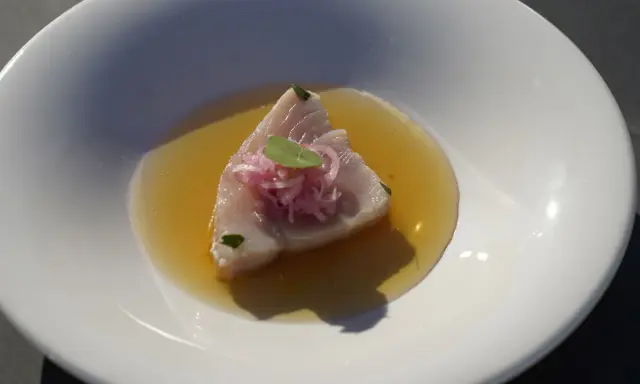 Bonito fresco en un caldo dorado, coronado con cebolla morada y una hoja verde. Un plato ligero y sabroso.