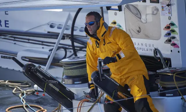 Skipper en tenue jaune, concentré, manœuvre un winch sur un bateau Banque Populaire.