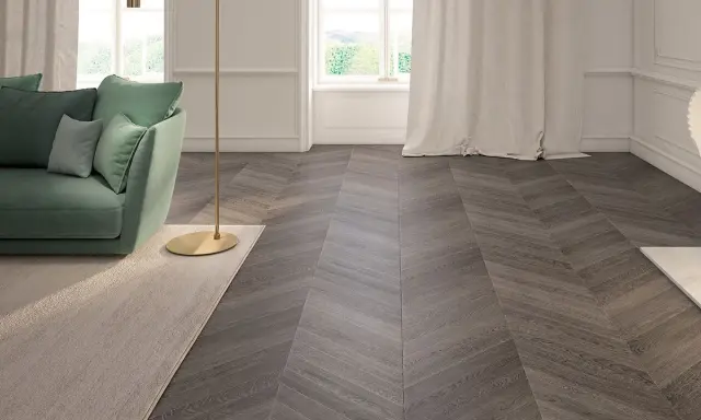 Elegante soggiorno con divano verde, lampada dorata e un tappeto beige. Il pavimento in parquet a spina di pesce, con un colore scuro e venature evidenti, completa l'arredamento.