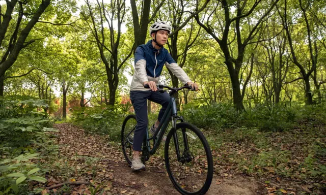 Mężczyzna w kasku jedzie rowerem trekkingowym po leśnej ścieżce. Taki rower to wszechstronny towarzysz podróży.