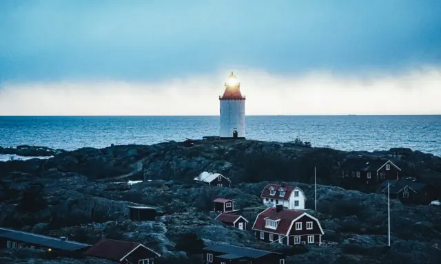 En fyr lyser över klippor och röda hus vid havet. En idyllisk plats för unika hotell Sverige.