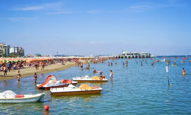 Spiaggia affollata a Gabicce, con ombrelloni colorati, gente in acqua e pedalò. Un'estate vivace al banana beach Gabicce.