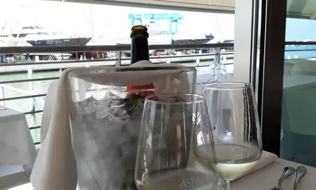 Un bicchiere di vino bianco e una bottiglia in un secchiello di ghiaccio, con vista sul porto e yacht, al ristorante club nautico Rimini.