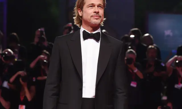Brad Pitt looking dapper in a classic tuxedo with a black cummerbund and bow tie, posing for photographers.