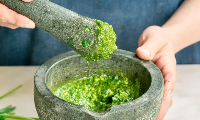 Frisches basilikum pesto wird in einem Mörser zerstoßen. Tropfen des grünen Pesto fallen vom Stößel in die Schüssel.