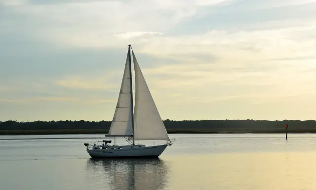 Un voilier blanc navigue sur une eau calme, ses voiles gonflées par le vent. La composition du bateau, avec la ligne d'horizon et le ciel doux, crée une scène paisible.