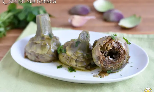 Tre carciofi alla romana cotti, serviti su un piatto bianco con prezzemolo tritato. Sullo sfondo, spicchi d'aglio e foglie di carciofo.