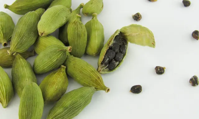 Gousses de cardamome verte, dont une ouverte révélant ses graines noires. Découvrez les cardamome bienfaits pour la santé et la cuisine.
