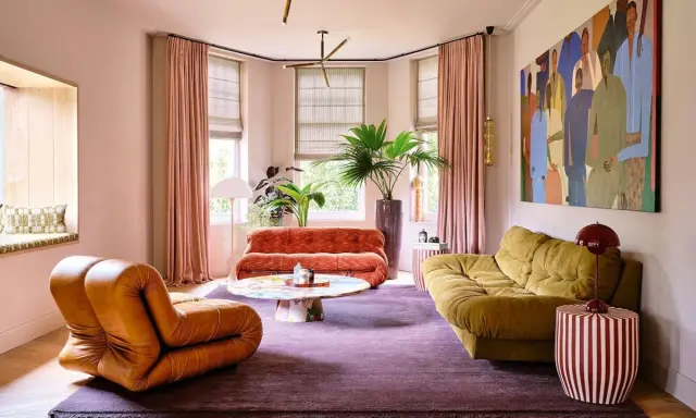 Comment amenager un salon : un fauteuil orange, un canapé rouille, un canapé moutarde, une table basse colorée, un tapis violet et une grande peinture.