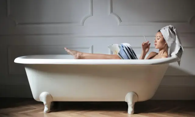 Kobieta relaksuje się w wannie, czytając i paląc. Zastanawiasz się, ile waży wanna żeliwna?
