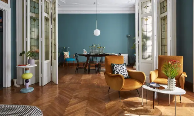 Un soggiorno che unisce con successo arredamento classico e moderno: sedie in velluto ocra, tavolino di design e porte antiche con vetri colorati.