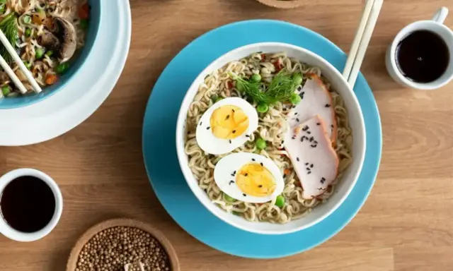 Miseczka z tantanmen, makaronem, jajkiem na twardo, plastrami mięsa i zielonym koperkiem. Obok sos sojowy i nasiona sezamu.