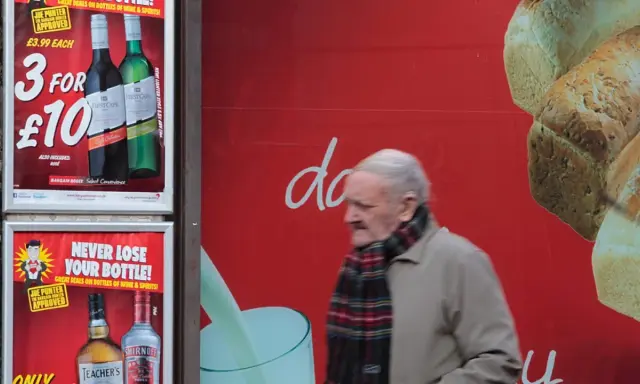 Starszy mężczyzna mija reklamę z promocją na alkohol. Włochy ceny alkoholu są atrakcyjne.