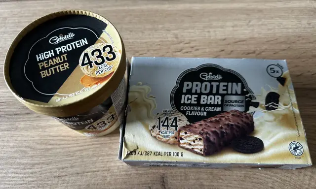 Gdzie kupić lody proteinowe? Na zdjęciu widać opakowania lodów Gelatelli: kubełek masło orzechowe i batoniki ciasteczkowe.