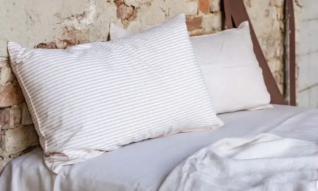 Cuscini a righe e tinta unita su un letto coperto da lenzuola di lino. Le caratteristiche del linone tessuto sono evidenti nella texture naturale.