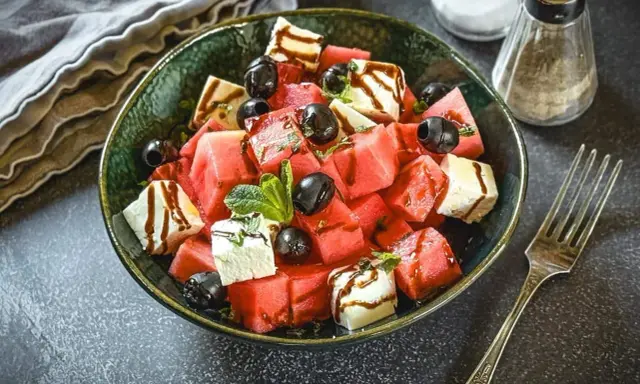 Erfrischender Melonen Feta Salat mit schwarzen Oliven und Minze, beträufelt mit Balsamico-Dressing. Perfekt für heiße Tage!
