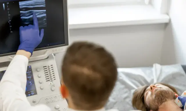 Lekarz wykonuje badanie doppler tętnic mózgowych, analizując obraz na monitorze USG.