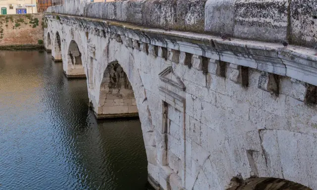 Il Ponte di Tiberio a Rimini, con i suoi archi in pietra bianca che si specchiano sull'acqua scura, testimonia secoli di storia.