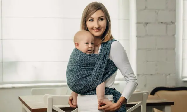 Uśmiechnięta mama nosi dziecko w chuście tkanej, która zapewnia komfort i bezpieczeństwo.