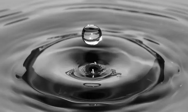Goutte d'eau en suspension au-dessus de son impact, créant des ondulations. L'eau calcaire reflète la lumière.
