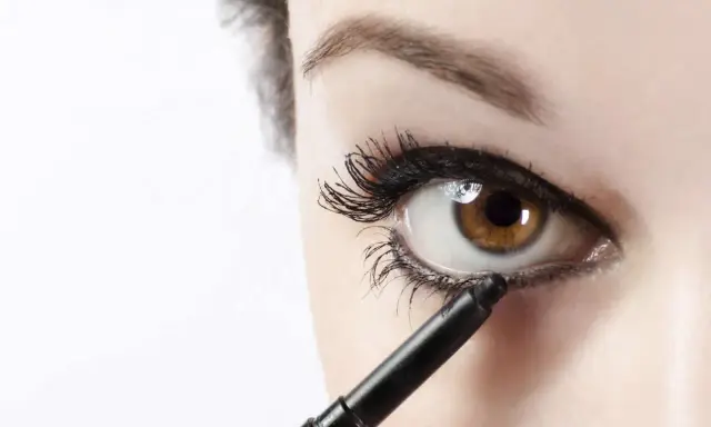 Ojo marrón recibiendo el toque final de maquillaje ojos negro con un lápiz.
