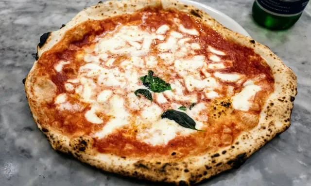 Pyszna pizza napoletana z rozpływającym się serem mozzarella i aromatycznym sosem pomidorowym, ozdobiona świeżą bazylią.