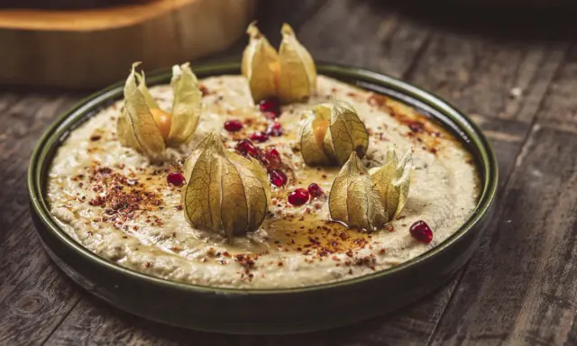 En krämig baba ganoush toppad med physalis och granatäppelkärnor på en rustik träyta.