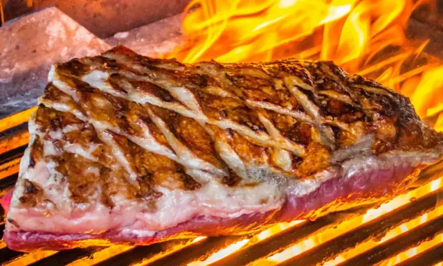 Jugosa viande de kobe a la parrilla, con marcas doradas y llamas naranjas danzando alrededor.