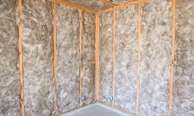 Coin d'une pièce en construction, murs et plafond recouverts d'isolation ouate de cellulose, structure en bois visible.