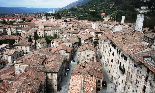Panoramica di tetti rossi e antichi edifici in pietra, con torri medievali che svettano. Un paesaggio che ricorda l'Umbria, tra Assisi e Gubbio.