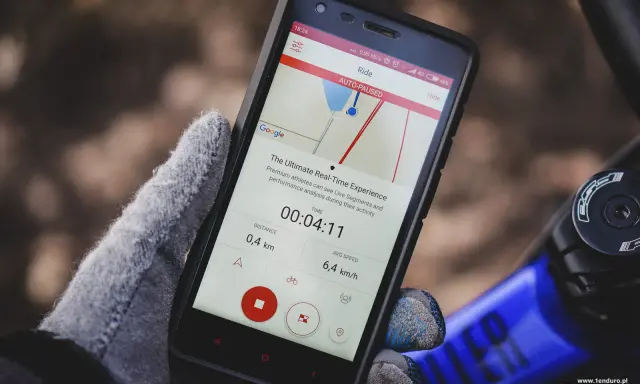 Rękawiczka trzyma smartfon z aplikacją licznik rowerowy. Widoczny czas 00:04:11, dystans 0,4 km i średnia prędkość 6,4 km/h.