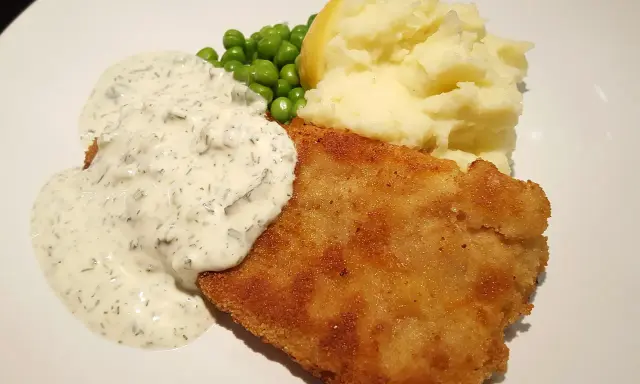 En gyllene panerad fisk med krämig sås, len potatismos, gröna ärtor och en citronklyfta. En klassisk och god måltid.