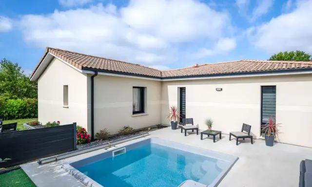 Vue aérienne d'une maison moderne avec piscine, le **plan maison en L** est bien visible, entouré de verdure.