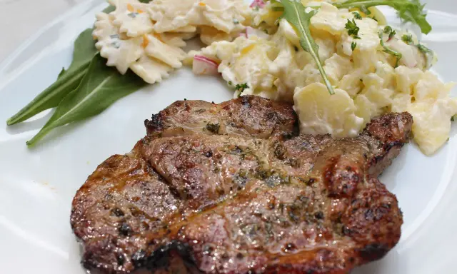 Saftiges Nackensteak grillen mit Kartoffel- und Nudelsalat auf einem weißen Teller.