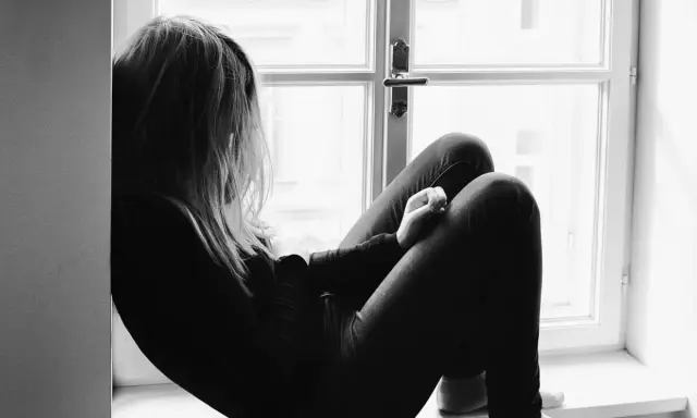 Una joven sentada en la ventana, con la mirada perdida. Un momento para reflexionar sobre qué decirle a tu hija cuando le rompen el corazón.