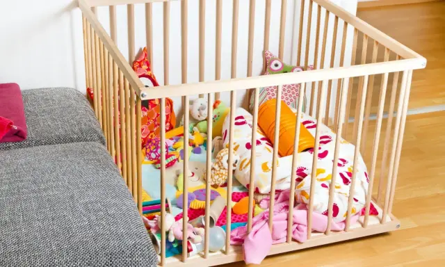 Ein bunter Spielteppich mit vielen Kuscheltieren und Kissen in einem Laufstall. Ja oder nein, diese sichere Spielzone für Babys?
